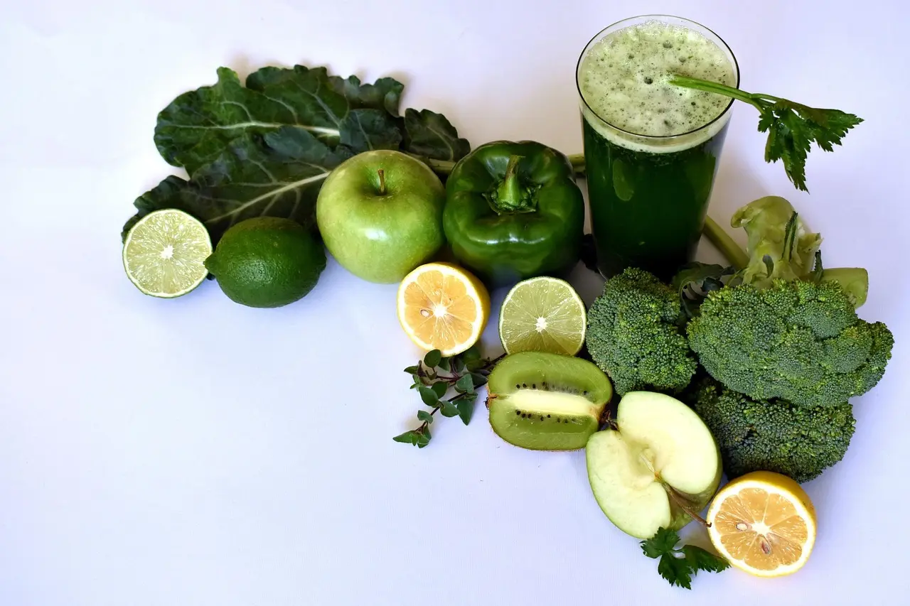 Grøn smoothie omgivet af æble, kiwi, lime og bladgrønt