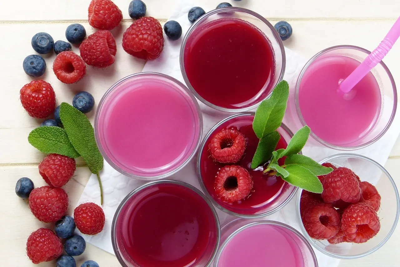 Pinkrøde smoothies i glas med friske hindbær og blåbær omkring